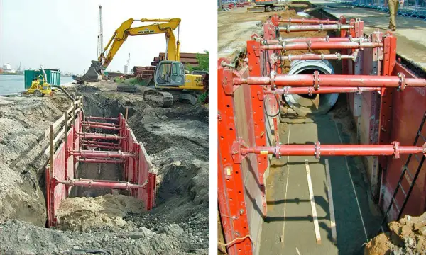 Excavación con entibación ligera para instalar tuberías. Maquinaria pesada y sistema de soporte rojo aseguran el área.