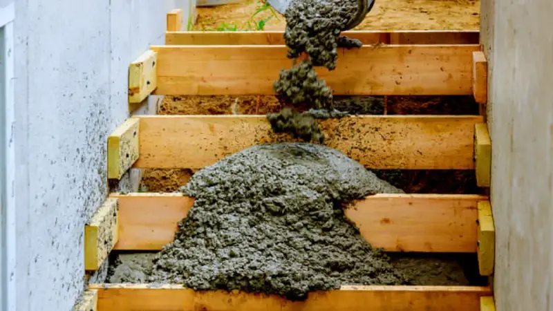 Vertiendo cemento en encofrado de madera para como hacer escalera de obra.